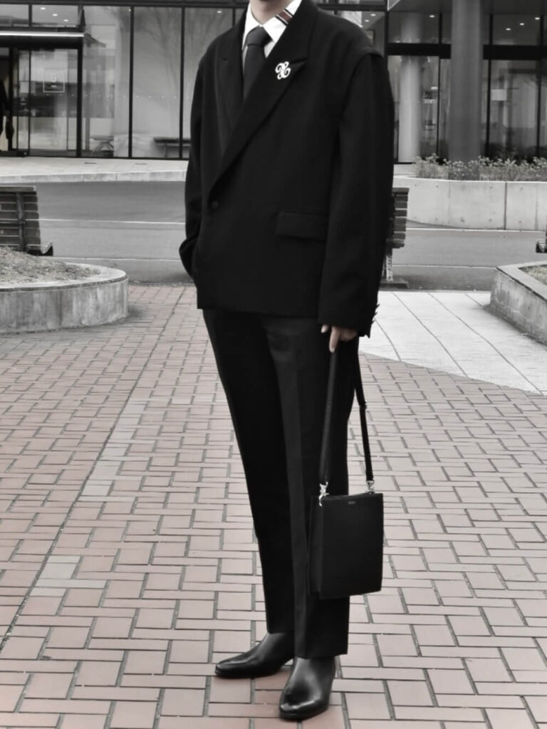黒のスーツセットアップ×白のタイラインシャツ×ボルドーのネクタイ×黒のブーツ